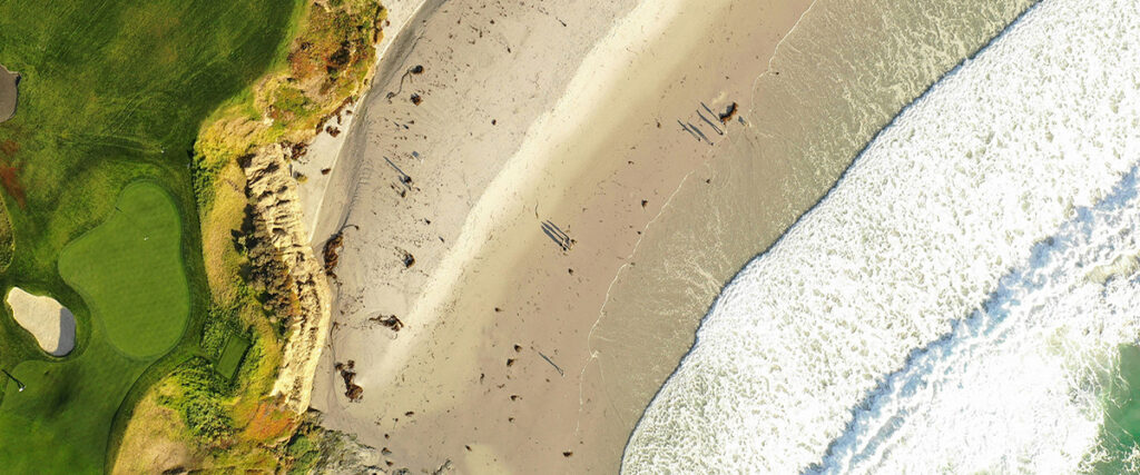 Golfplatz an der Küste mit Sandstrand und Meereswellen aus der Vogelperspektive – Traumziel für Golfreisen.